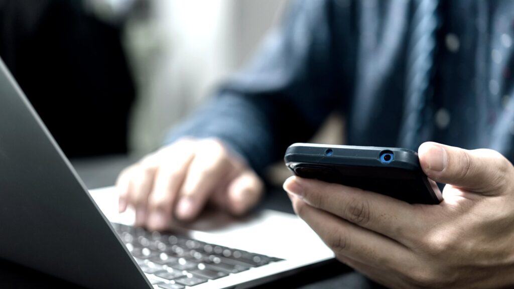 ノートPCの前でスマートフォンを操作する手元